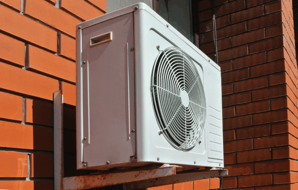 Wall-mounted air conditioner compressor unit attached to a red brick exterior.