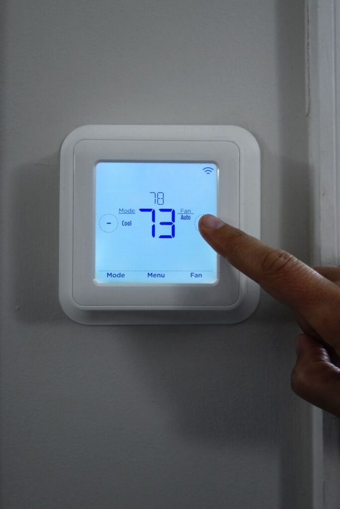 Digital wall thermostat displaying 73 degrees with hand adjusting temperature